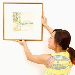 Rear view of a young woman mounting a picture frame on the wall and smiling